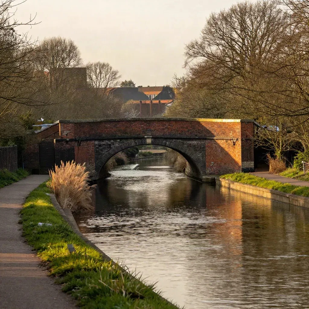 Amber West Midlands canal with brick bridge, trees, and soft haze over calm water.